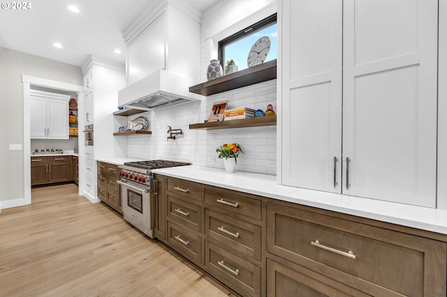 kitchen with white cabinetry, stainless steel appliances, light hardwood / wood-style floors, custom range hood, and decorative backsplash