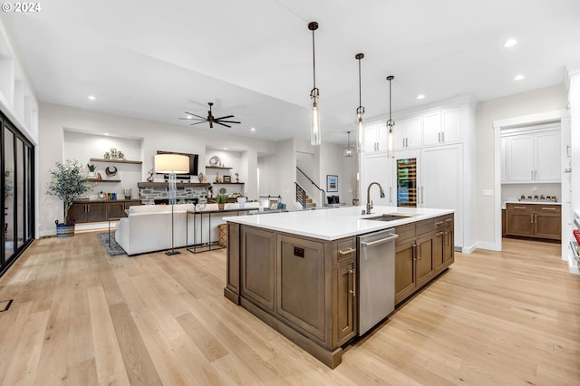 kitchen with sink, hanging light fixtures, light hardwood / wood-style floors, a center island with sink, and stainless steel dishwasher