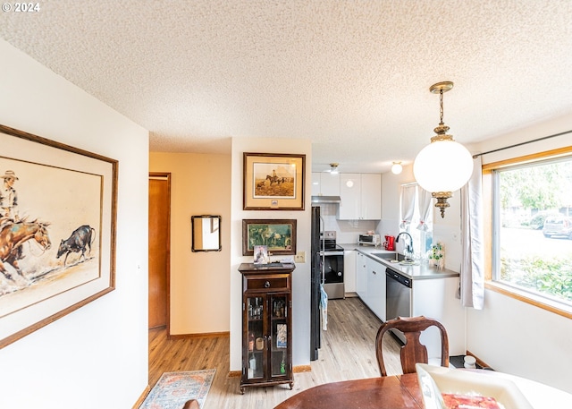 kitchen with a textured ceiling, white cabinetry, light hardwood / wood-style flooring, hanging light fixtures, and appliances with stainless steel finishes