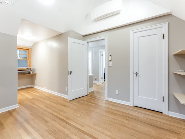 interior space with an AC wall unit, lofted ceiling, and light wood-type flooring