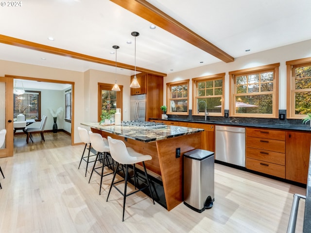 kitchen featuring light wood-type flooring, dark stone counters, stainless steel appliances, pendant lighting, and a kitchen island