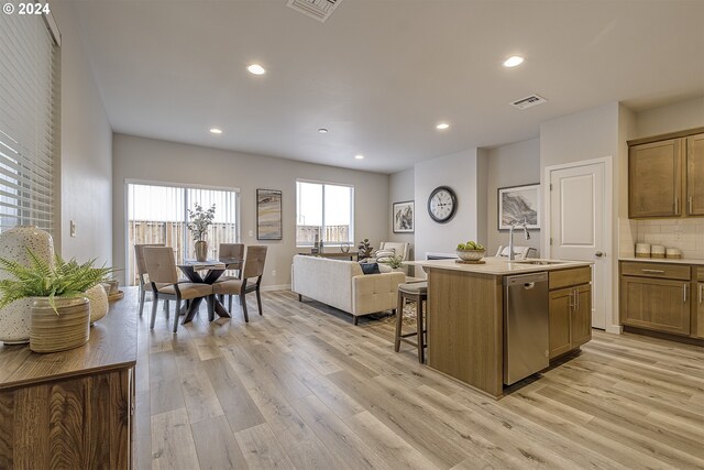 kitchen with sink, dishwasher, a kitchen island with sink, tasteful backsplash, and light wood-type flooring