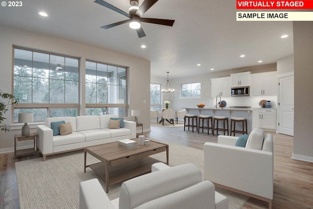 living room with ceiling fan with notable chandelier, light wood-type flooring, plenty of natural light, and sink