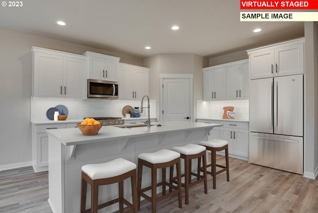 kitchen with an island with sink, white cabinetry, light hardwood / wood-style flooring, and stainless steel appliances