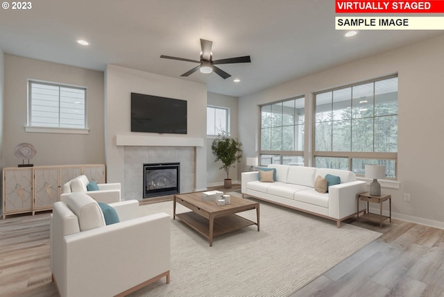 living room featuring light hardwood / wood-style flooring, ceiling fan, and a tile fireplace