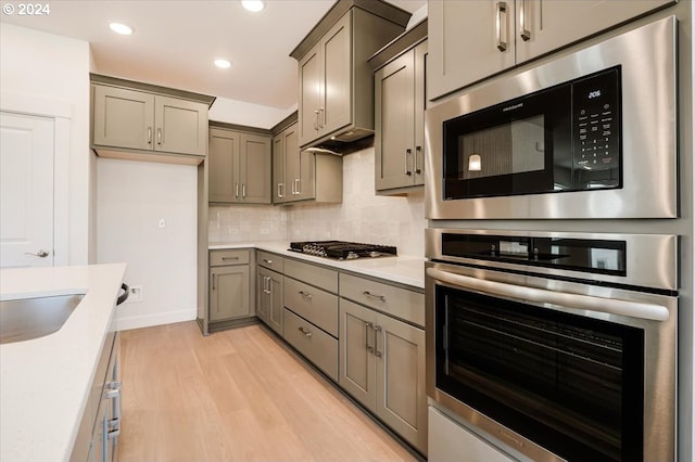 kitchen with appliances with stainless steel finishes, light wood-type flooring, tasteful backsplash, and sink