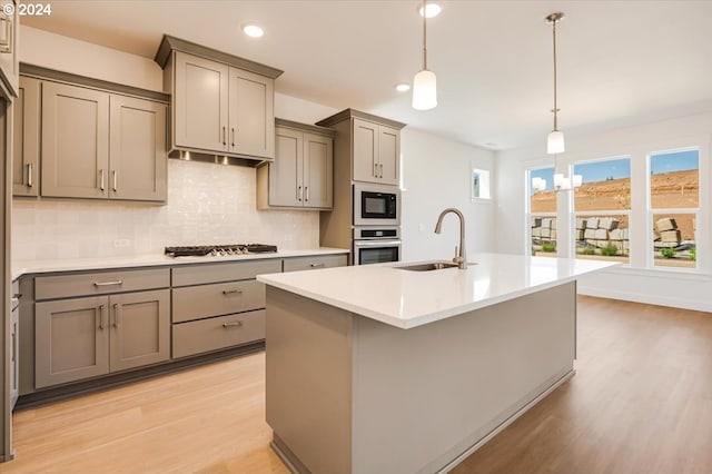 kitchen featuring a center island with sink, sink, light wood-type flooring, tasteful backsplash, and stainless steel appliances