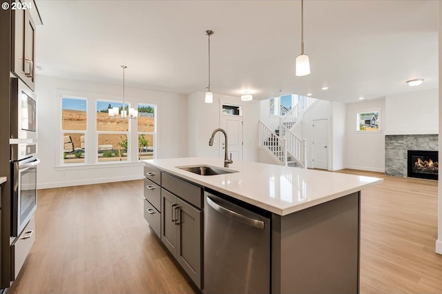 kitchen featuring appliances with stainless steel finishes, sink, decorative light fixtures, light hardwood / wood-style flooring, and an island with sink