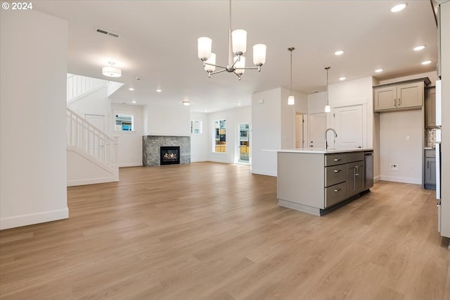 kitchen with gray cabinetry, a kitchen island with sink, decorative light fixtures, light hardwood / wood-style floors, and a stone fireplace