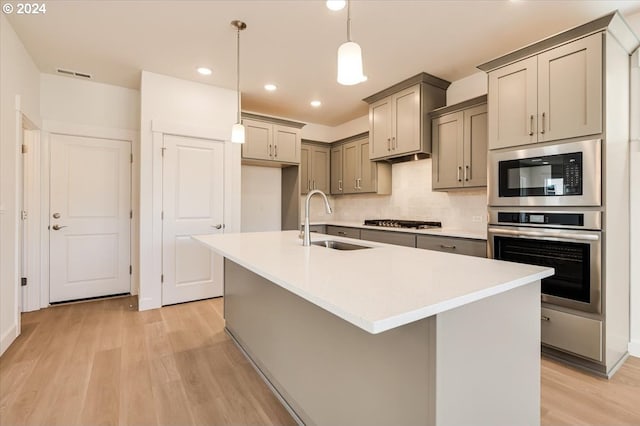 kitchen featuring appliances with stainless steel finishes, light hardwood / wood-style floors, hanging light fixtures, and a center island with sink