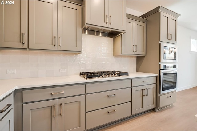 kitchen with gray cabinetry, decorative backsplash, stainless steel appliances, and light hardwood / wood-style flooring