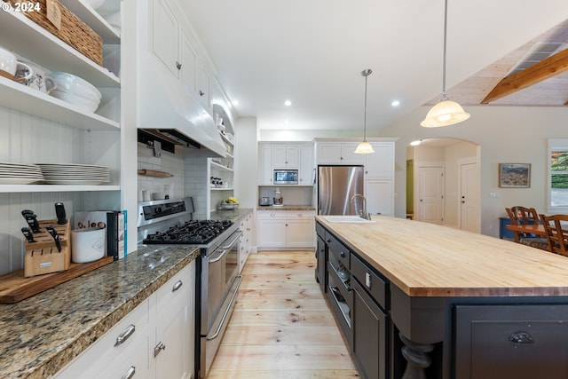 kitchen featuring appliances with stainless steel finishes, a center island with sink, white cabinets, and butcher block countertops