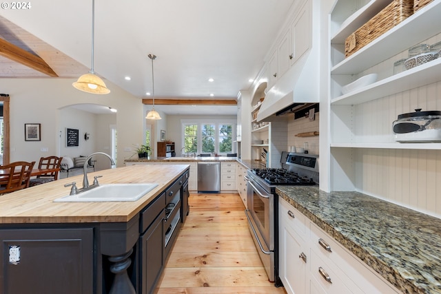 kitchen featuring decorative light fixtures, appliances with stainless steel finishes, a kitchen island with sink, sink, and white cabinetry