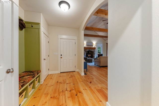 entryway featuring a stone fireplace, hardwood / wood-style floors, and beam ceiling