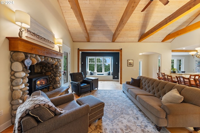 living room with ceiling fan with notable chandelier, vaulted ceiling with beams, wooden ceiling, and a stone fireplace