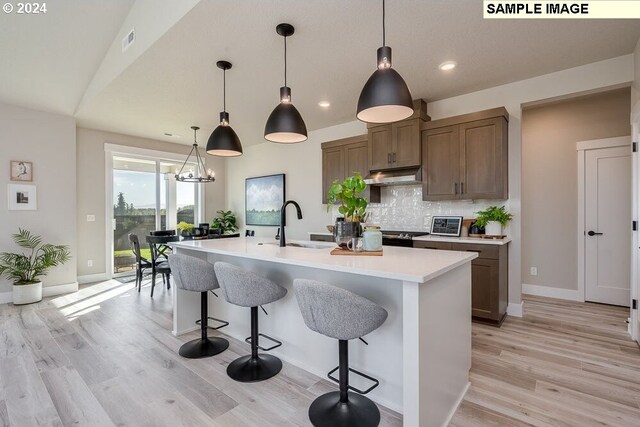 kitchen featuring an island with sink, decorative light fixtures, light hardwood / wood-style floors, and tasteful backsplash