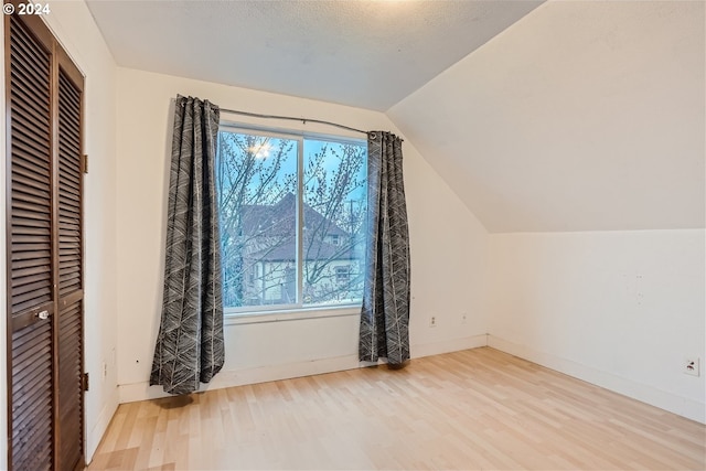 bonus room with lofted ceiling, a textured ceiling, and light wood-type flooring