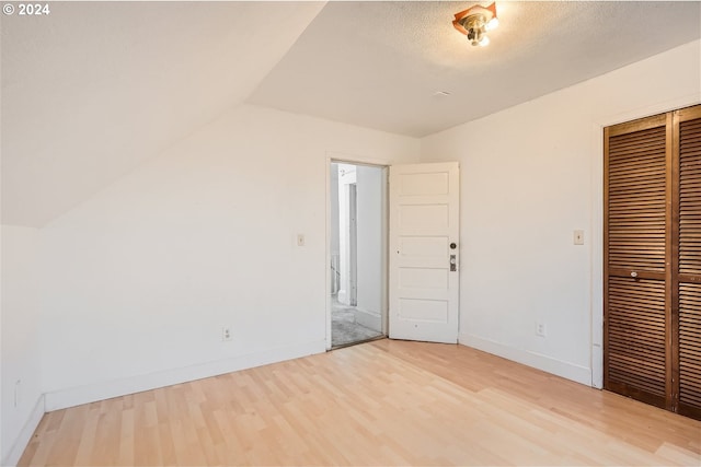 unfurnished bedroom with lofted ceiling, a closet, and light wood-type flooring