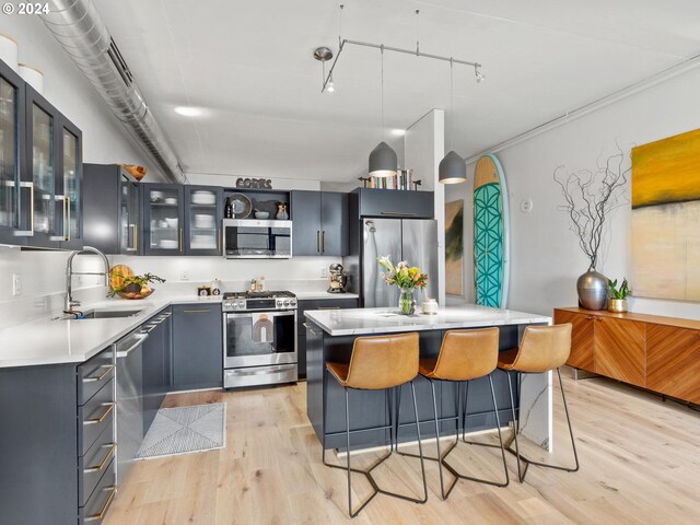 kitchen featuring sink, light hardwood / wood-style flooring, decorative light fixtures, a kitchen island, and appliances with stainless steel finishes