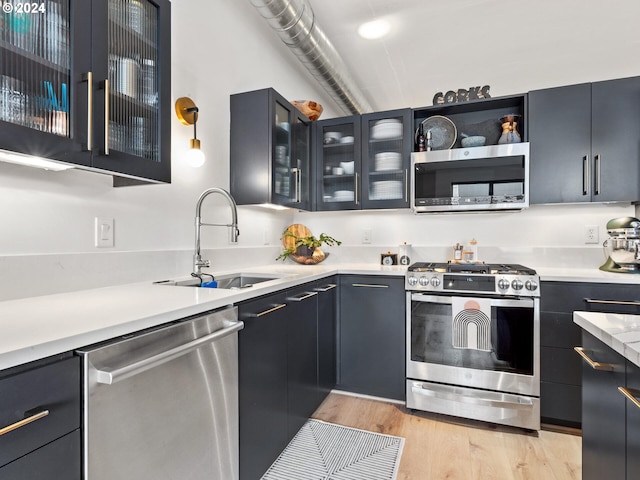 420 NW 11th Ave Unit 502, Portland, OR 97209 - kitchen featuring appliances with stainless steel finishes, a sink, light wood-type flooring, light countertops, and glass insert cabinets