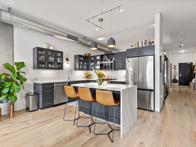 kitchen with appliances with stainless steel finishes, a kitchen island, light hardwood / wood-style flooring, and pendant lighting