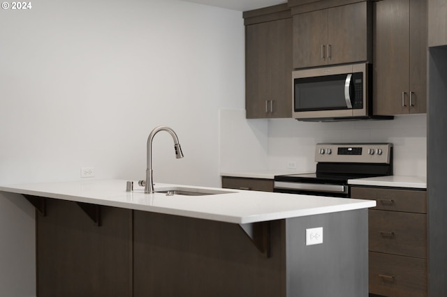 kitchen featuring kitchen peninsula, a kitchen bar, dark brown cabinetry, stainless steel appliances, and sink