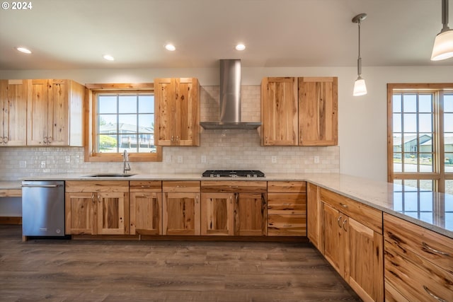 kitchen with wall chimney range hood, sink, decorative light fixtures, light stone counters, and stainless steel appliances