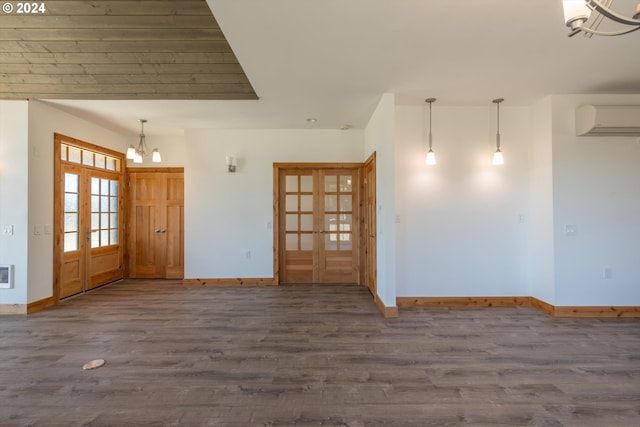 empty room with a wall mounted air conditioner, french doors, dark hardwood / wood-style flooring, and an inviting chandelier