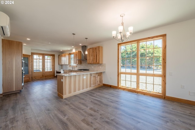 kitchen with kitchen peninsula, tasteful backsplash, wall chimney exhaust hood, pendant lighting, and an inviting chandelier