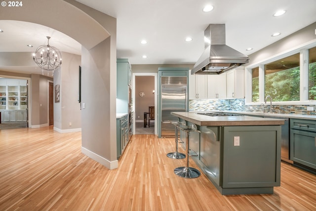 kitchen featuring hanging light fixtures, island exhaust hood, appliances with stainless steel finishes, a kitchen island, and light wood-type flooring