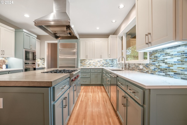 kitchen with island exhaust hood, stainless steel appliances, sink, white cabinets, and light hardwood / wood-style floors