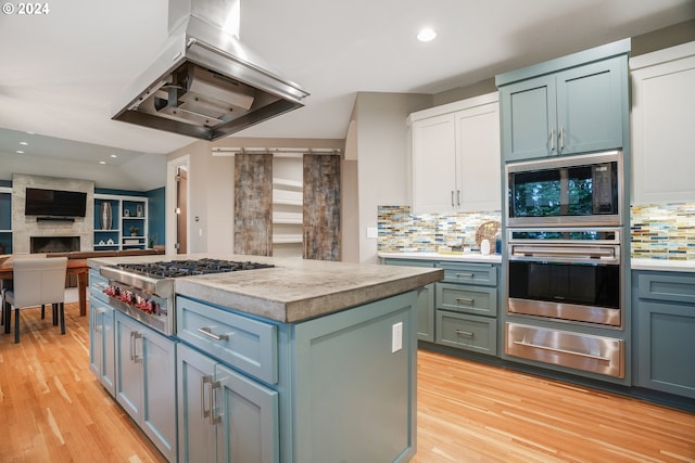 kitchen with light hardwood / wood-style flooring, tasteful backsplash, a kitchen island, island exhaust hood, and stainless steel gas cooktop