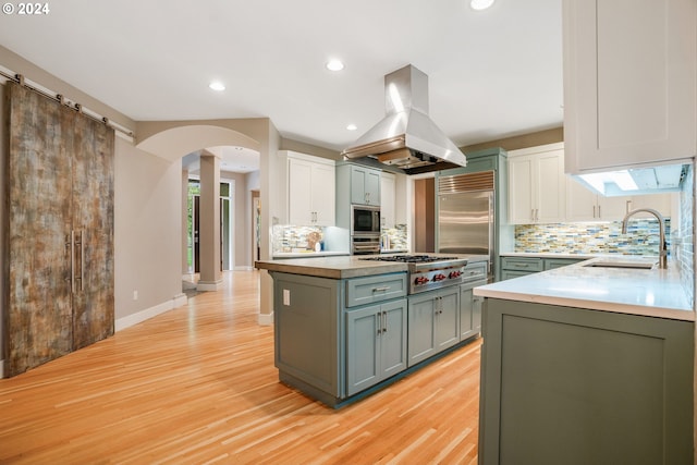 kitchen featuring sink, built in appliances, decorative backsplash, island range hood, and light wood-type flooring