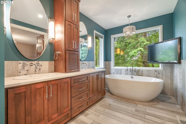 bathroom featuring an inviting chandelier, hardwood / wood-style floors, a bathtub, vanity, and tile walls