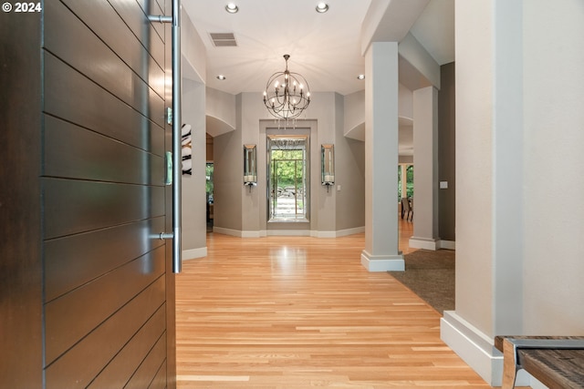 entrance foyer featuring light wood-type flooring, ornate columns, and a notable chandelier