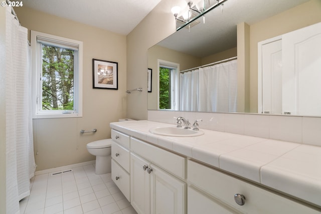 bathroom with toilet, vanity, tile patterned floors, and a healthy amount of sunlight