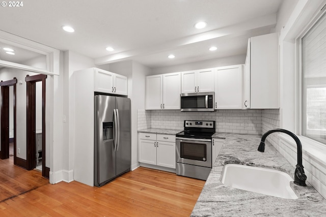 kitchen with light stone counters, stainless steel appliances, sink, and white cabinets