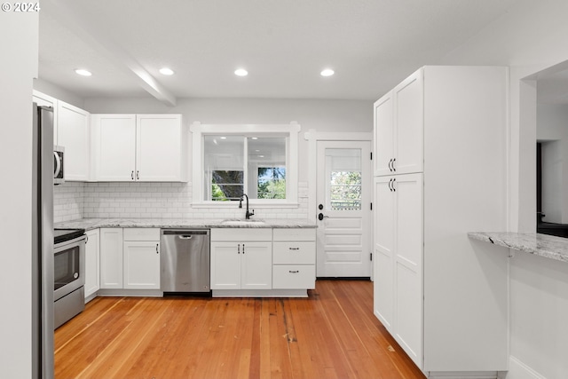 kitchen with light stone countertops, appliances with stainless steel finishes, white cabinets, and decorative backsplash