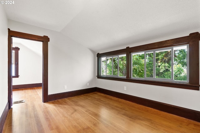 empty room featuring vaulted ceiling, light hardwood / wood-style flooring, and a textured ceiling