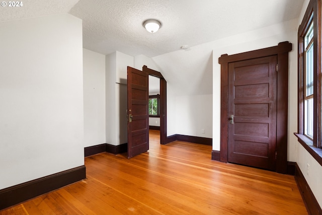 spare room with light hardwood / wood-style flooring, vaulted ceiling, a textured ceiling, and plenty of natural light