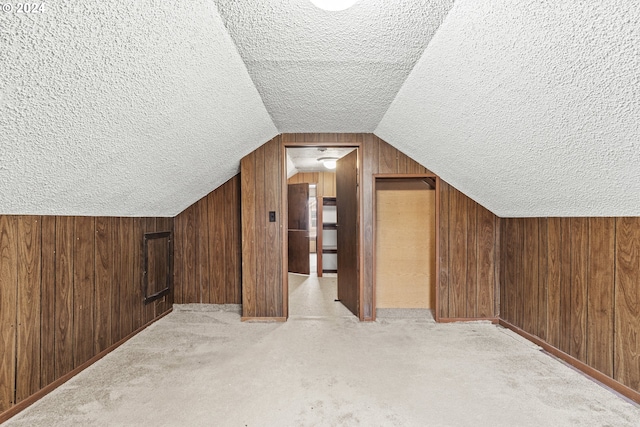 additional living space with a textured ceiling, light colored carpet, vaulted ceiling, and wooden walls