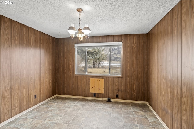 5851 Wocus Rd, Klamath Falls, OR 97601 - empty room with a chandelier, stone finish flooring, a textured ceiling, wooden walls, and baseboards