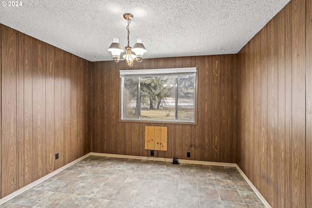 empty room with wood walls, a chandelier, and a textured ceiling