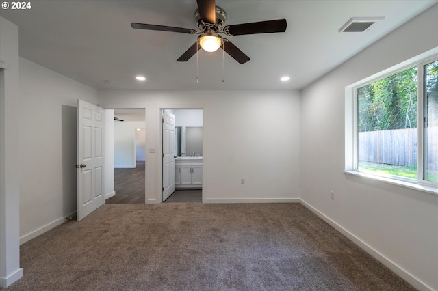 unfurnished bedroom with dark colored carpet, connected bathroom, ceiling fan, and sink