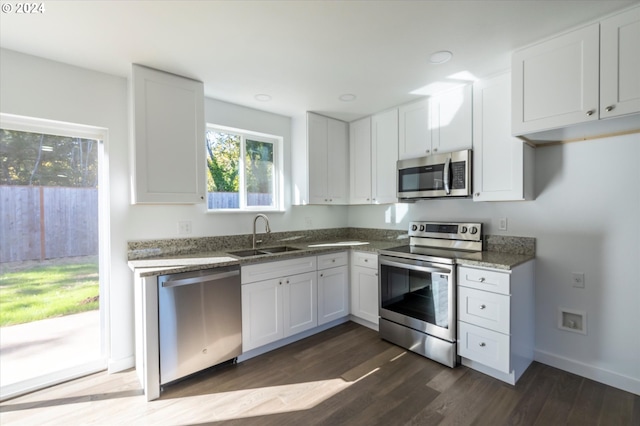 kitchen with stainless steel appliances, sink, dark stone countertops, white cabinets, and dark hardwood / wood-style floors