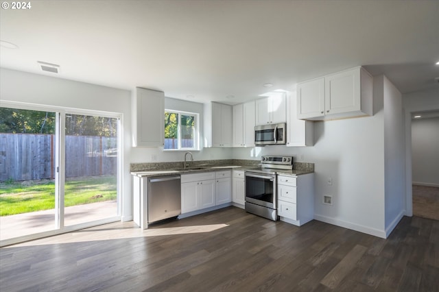 kitchen featuring appliances with stainless steel finishes, dark wood-style flooring, a sink, white cabinets, and baseboards