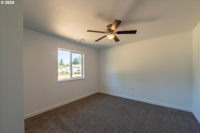 empty room with dark colored carpet, a ceiling fan, and baseboards