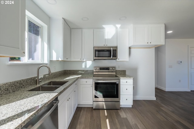 kitchen featuring stainless steel appliances, a sink, light stone counters, dark wood-style floors, and white cabinets