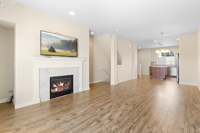 unfurnished living room featuring an inviting chandelier, a tile fireplace, and light hardwood / wood-style flooring