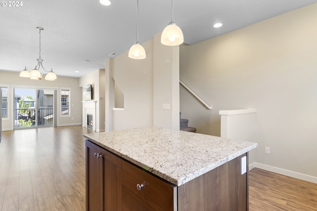 kitchen featuring a kitchen island, decorative light fixtures, light stone countertops, a chandelier, and light hardwood / wood-style flooring